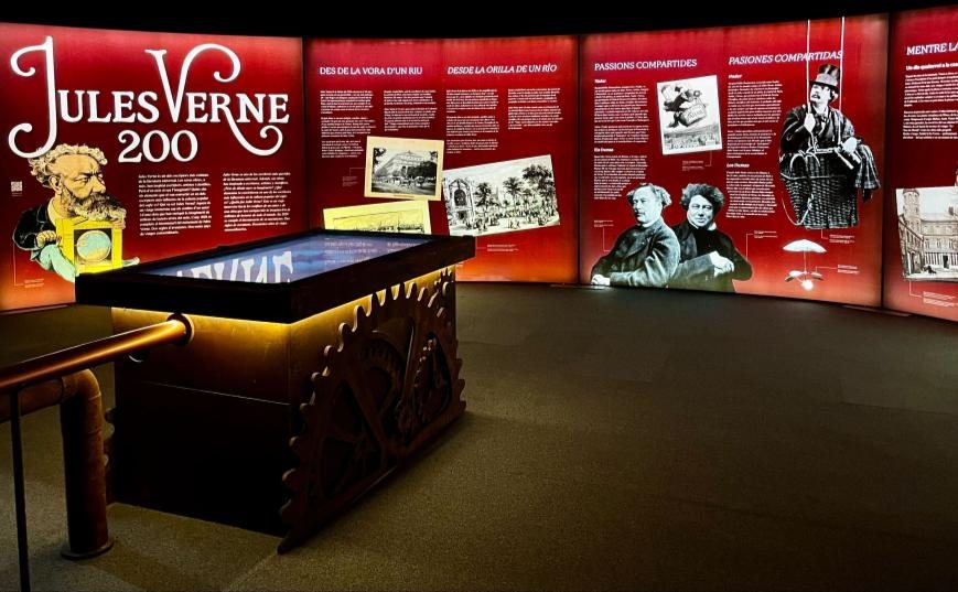 Room 01, Jules Verne: A Curious Spirit — red exhibition panels on Verne's life around a steampunk interactive table