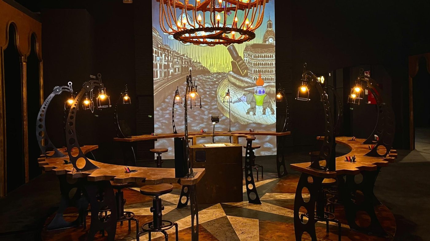 Room 05, Les Machines Verniennes — the Sketch & Post room with steampunk lamps and drawing tables in front of a giant animated screen of Nantes